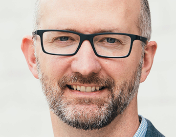 Dr. Patrick Kirchen smiles at the camera. He has black glasses and a short beard.